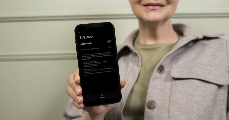 A woman holds a smartphone displaying the TalkBack accessibility settings on its screen.