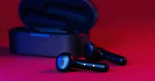 This image features a pair of black wireless earbuds with LED indicators lying outside of their open charging case, all set against a vivid red background.