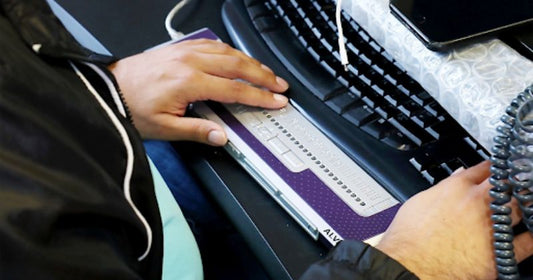 A person using a braille keyboard for a computer, with their hands placed on the raised-dot input keys.