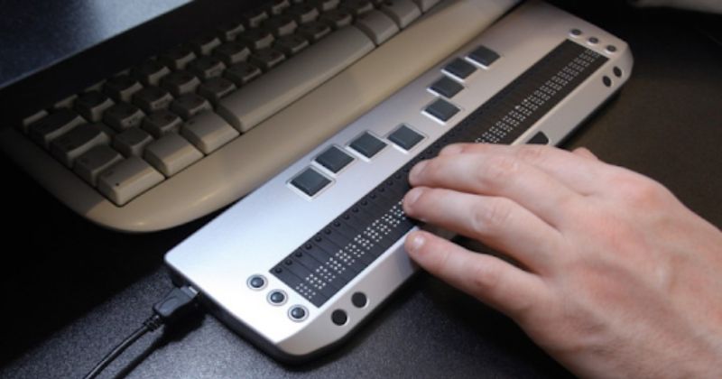 A user typing on a keyboard for blind people, featuring raised tactile keys and Braille input. 