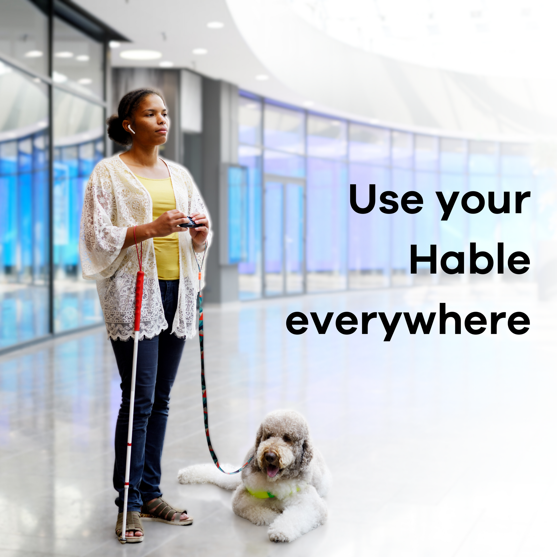 A visually impaired woman with her guide dog in a public space, standing and typing on her phone with her Hable One while her phone is in her pocket.