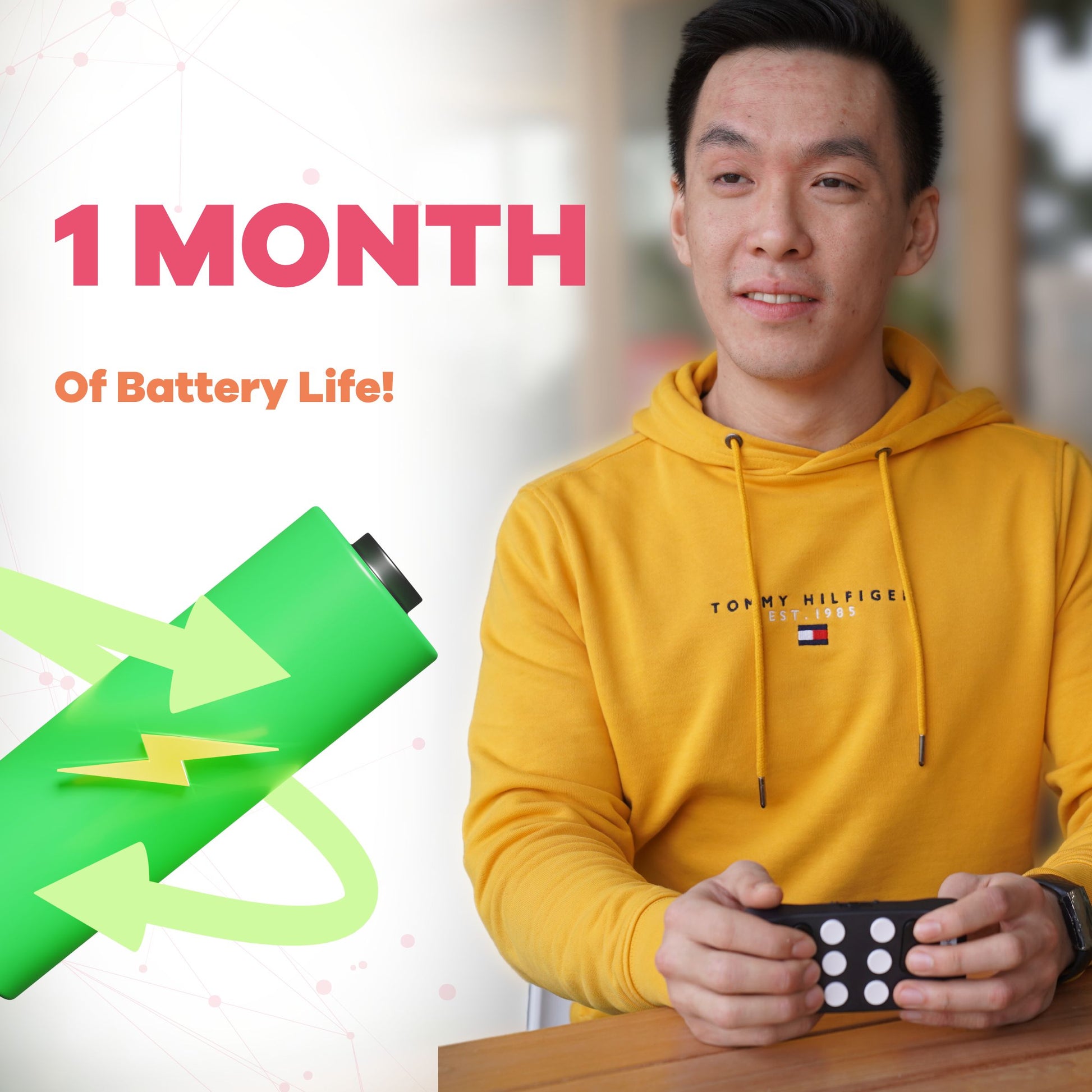 The image shows a man sitting at a table holding a Hable One Braille keyboard. He is smiling and wearing a yellow hoodie. To the left of him is an illustration of a green battery with a lightning bolt and circular arrows, symbolizing long battery life. The text above reads, "1 MONTH of Battery Life!" indicating that the Hable One device can last up to a month on a single charge.